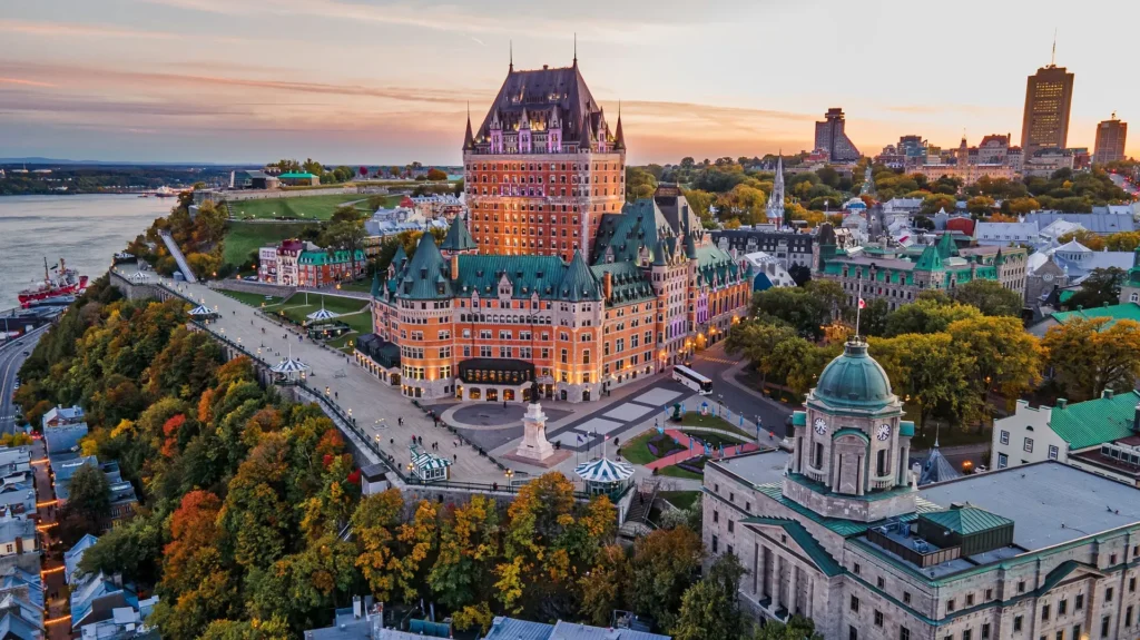Aerial view of Old Quebec at sunset featuring Fairmont Le Château Frontenac and the Dufferin Terrace along the St. Lawrence River.