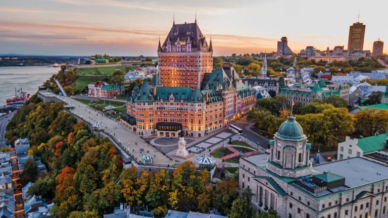 Aerial view of Old Quebec at sunset featuring Fairmont Le Château Frontenac and the Dufferin Terrace along the St. Lawrence River.